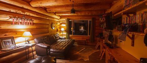 Interior acogedor de una cabaña de troncos con un sofá de cuero, un sillón mecedor de madera y una estantería llena de libros.