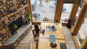 A wooden deck with a stone wall, a table with a laptop, and a view of outdoor seating.
