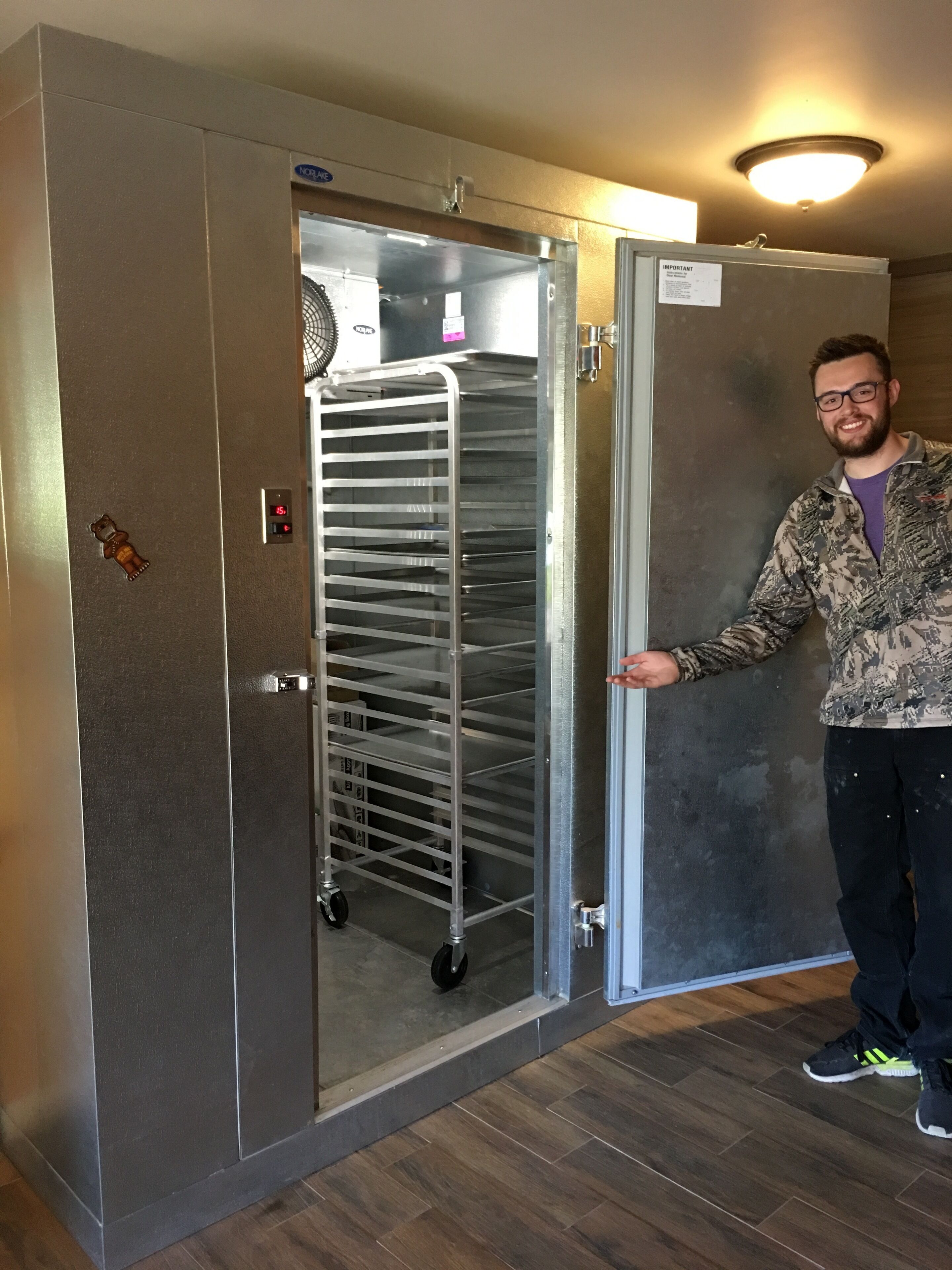 A man standing next to a walk-in refrigerator with a metal rack inside.