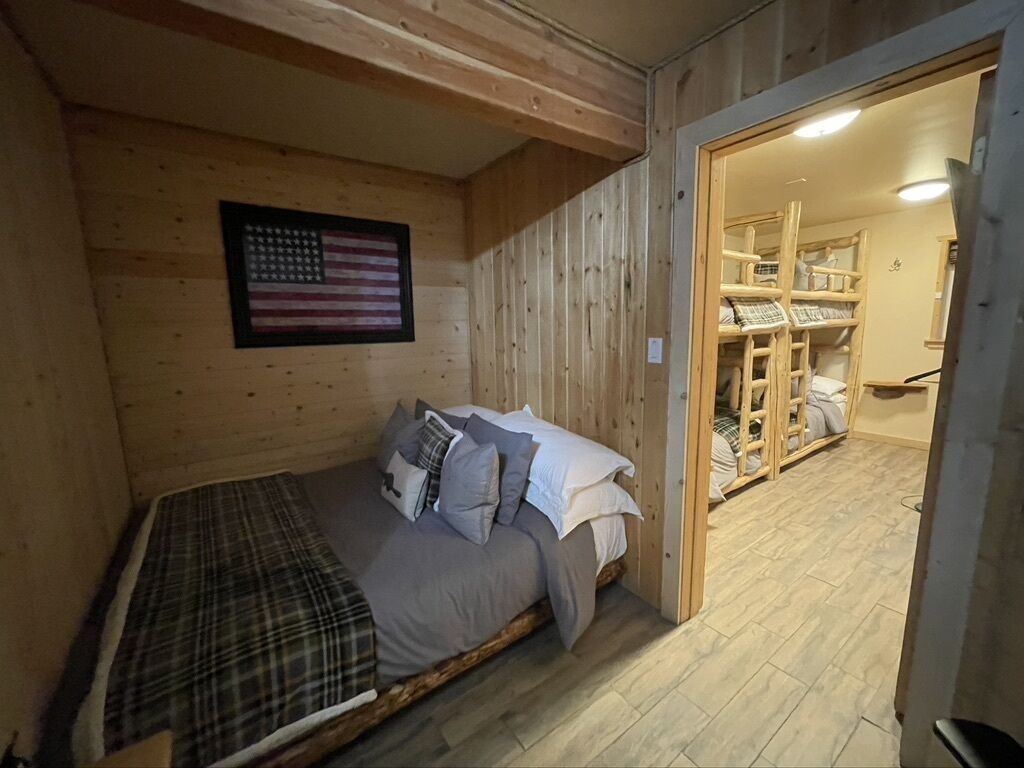 A wooden cabin room with a bed, a small table, and a shelf.