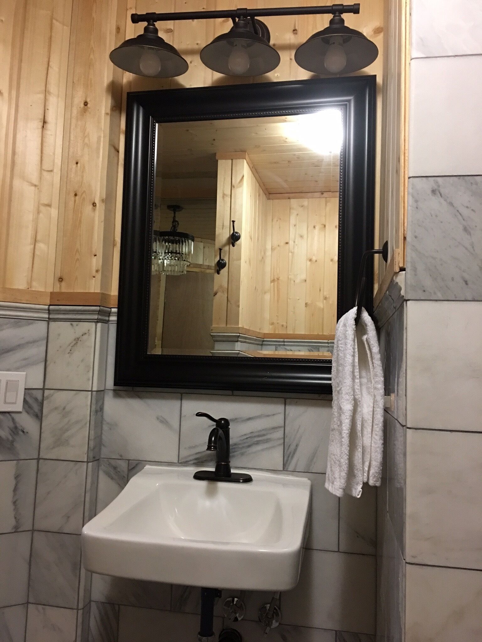 A bathroom with a white sink, a black-framed mirror, and wooden paneling on the walls.