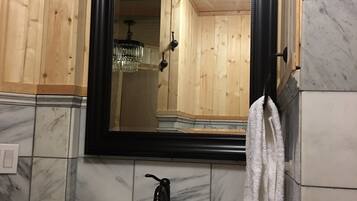 A bathroom with a white sink, a black-framed mirror, and wooden paneling on the walls.