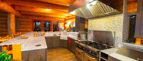 Une cuisine moderne dotée de meubles en bois, d’un grand îlot central, d’appareils électroménagers en acier inoxydable et d’un pare-feu en pierre.