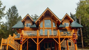 A log cabin with a balcony, wooden deck, and stone walls.