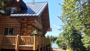 A log cabin with a porch, a view of a lake, and a flag.