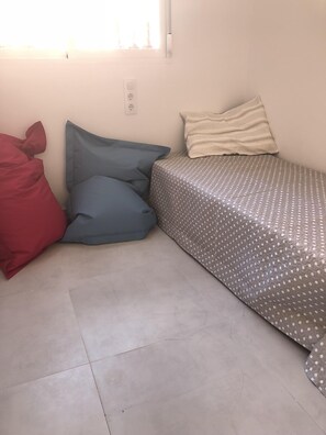 A small, single-bed room with a patterned bedspread, a red and blue blanket, and a window with a view of trees. - Dream holidays in an idyllic residence.  (Denia)