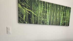 Un salon moderne avec un fauteuil blanc, un canapé foncé et une décoration murale représentant une forêt de bambous.