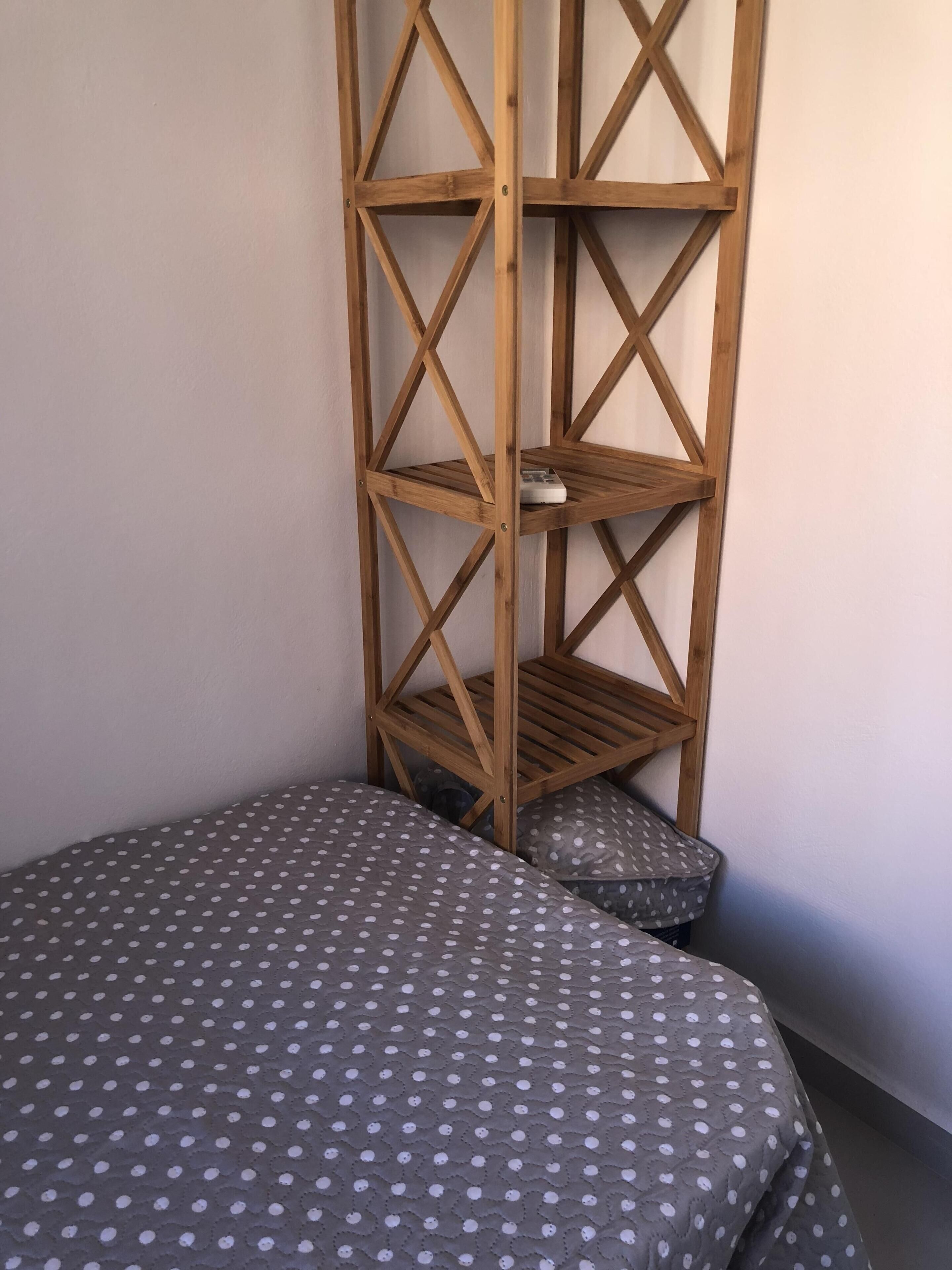 Una camera d'angolo con un letto, una scaffalatura in legno e un cuscino.