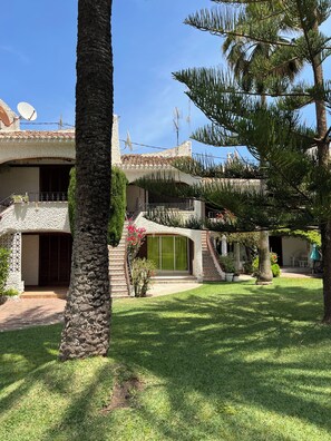 A courtyard with a stone building, a palm tree, and a well-maintained lawn.