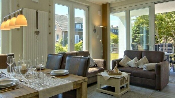 A spacious living room with a large window, a dining area with a table set for four, and a comfortable seating area with a sofa and armchairs.