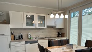 A modern kitchen with white cabinets, a built-in dishwasher, a coffee maker, and a dining area with a wooden table and leather chairs.