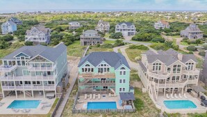 A coastal residential area with multiple houses featuring large balconies, swimming pools, and a well-maintained landscape. - Premier Oceanfront Dog Friendly Home w/ Pool, Hot Tub, EV Charger, and Game Room (Hatteras)
