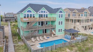 A multi-story beachfront property with a pool, outdoor seating, and a wooden deck. - Premier Oceanfront Dog Friendly Home w/ Pool, Hot Tub, EV Charger, and Game Room (Hatteras)
