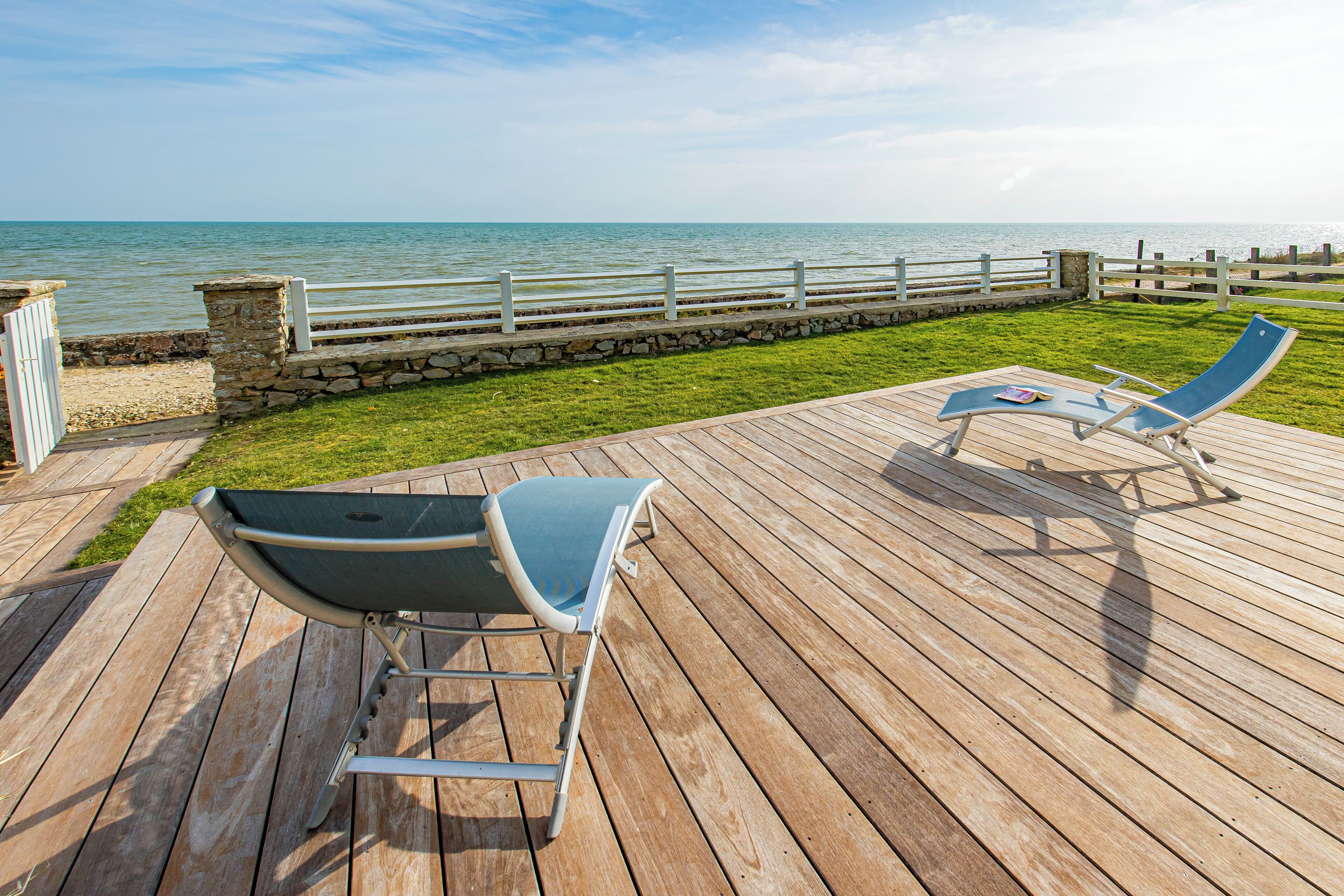 Une terrasse en bois avec deux chaises longues donnant sur un mur de pierre et offrant une vue sur l’océan.