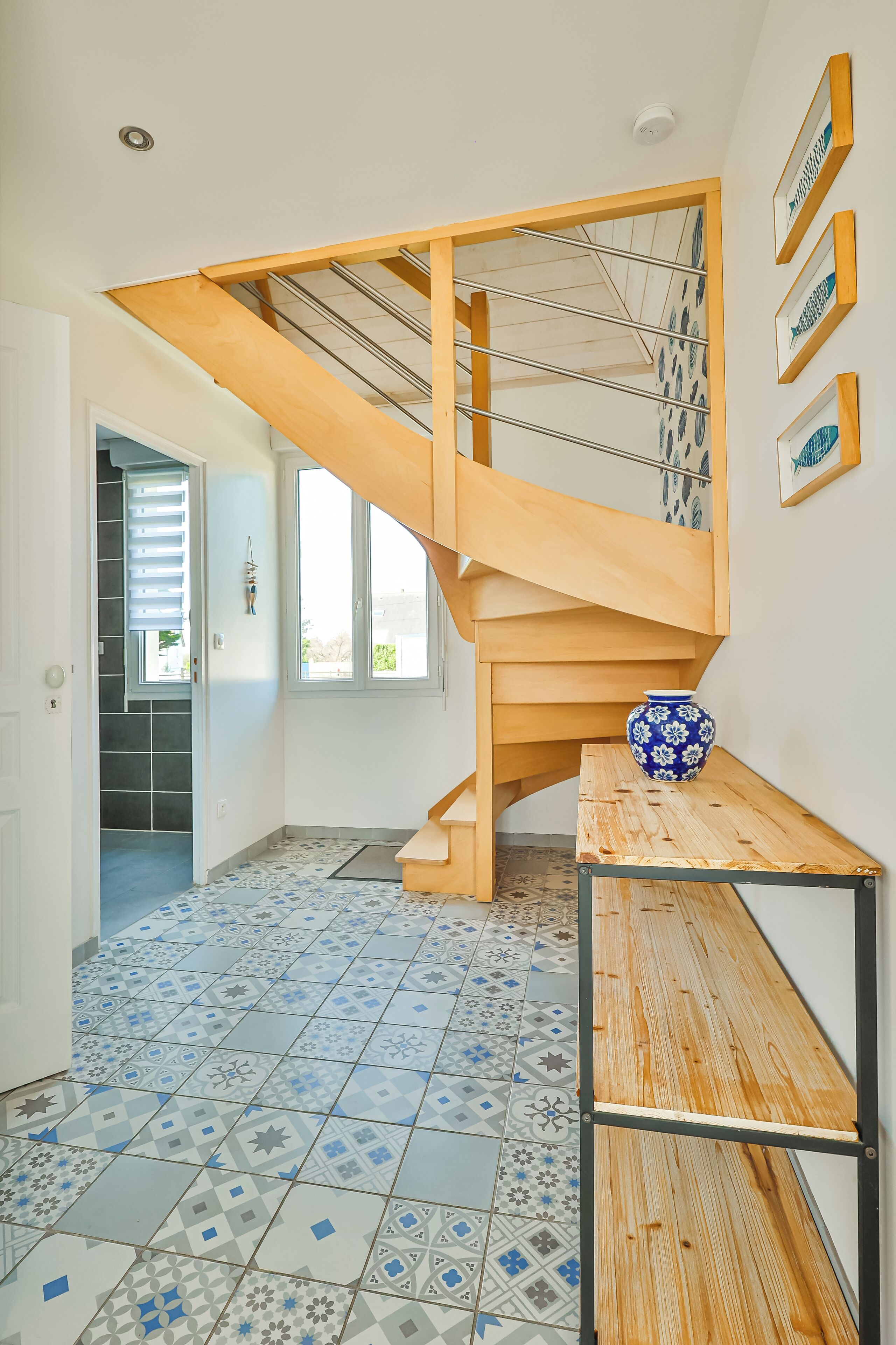 Un intérieur moderne avec un escalier en bois, un sol carrelé et un vase posé sur une table.