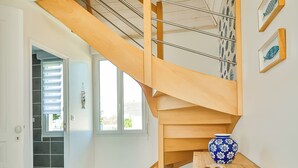 A modern interior with a wooden staircase, tiled floor, and a vase on a table.