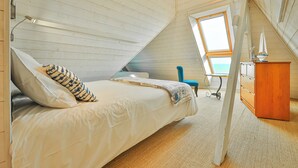A cozy attic bedroom with a bed, a desk, and a view of the outdoors.