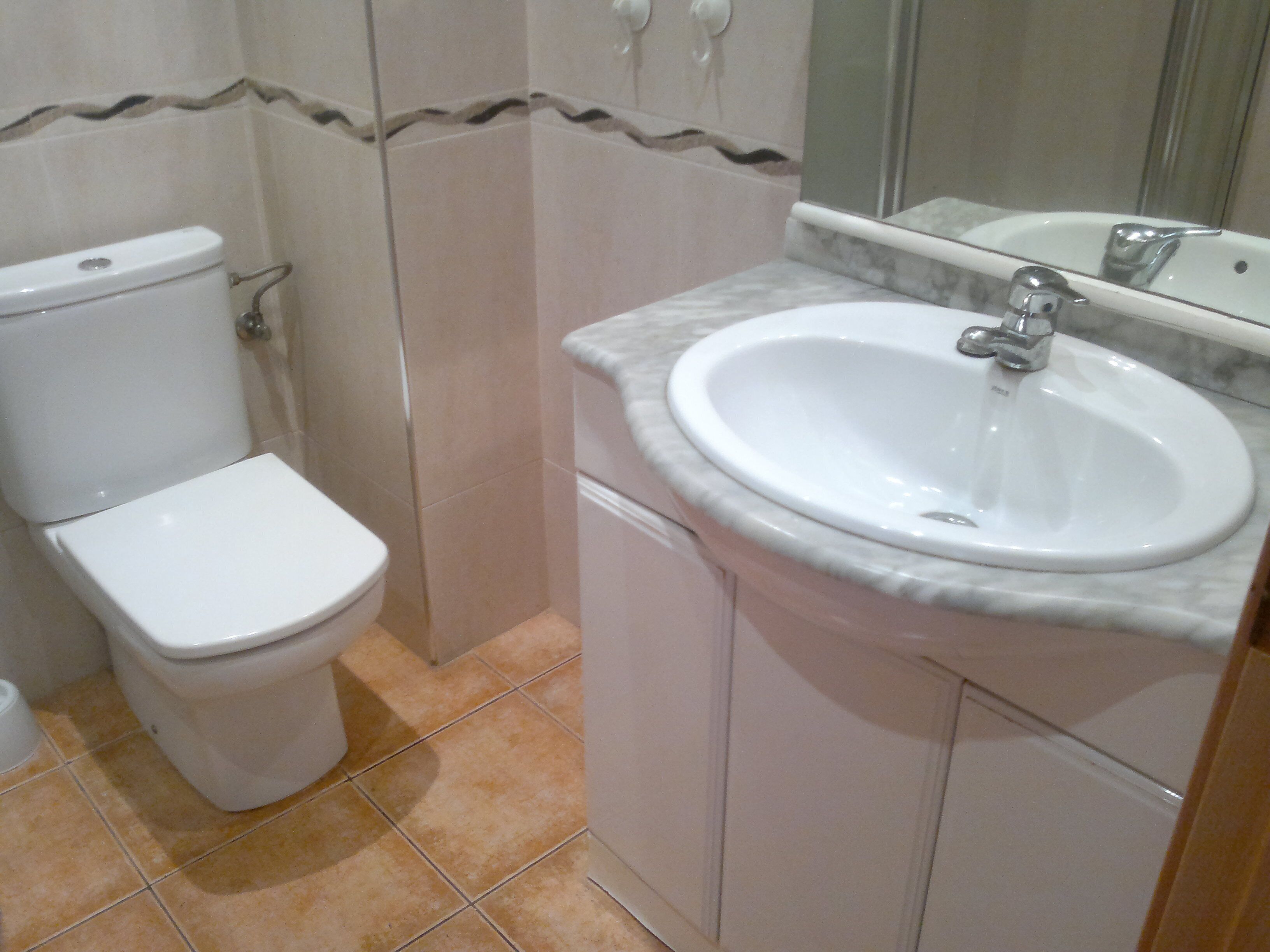 A bathroom with a toilet, sink, and mirror.