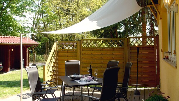 Un patio al aire libre con una mesa dispuesta para dos personas, rodeada de sillas, bajo una pérgola.