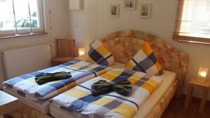 Una cama doble con cabecera floral, dos mesitas de noche con lámparas, un radiador y una ventana con persianas.