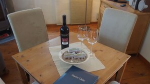 Una mesa de comedor de madera con una botella de vino, dos copas de vino, un plato de bombones y un libro azul titulado 