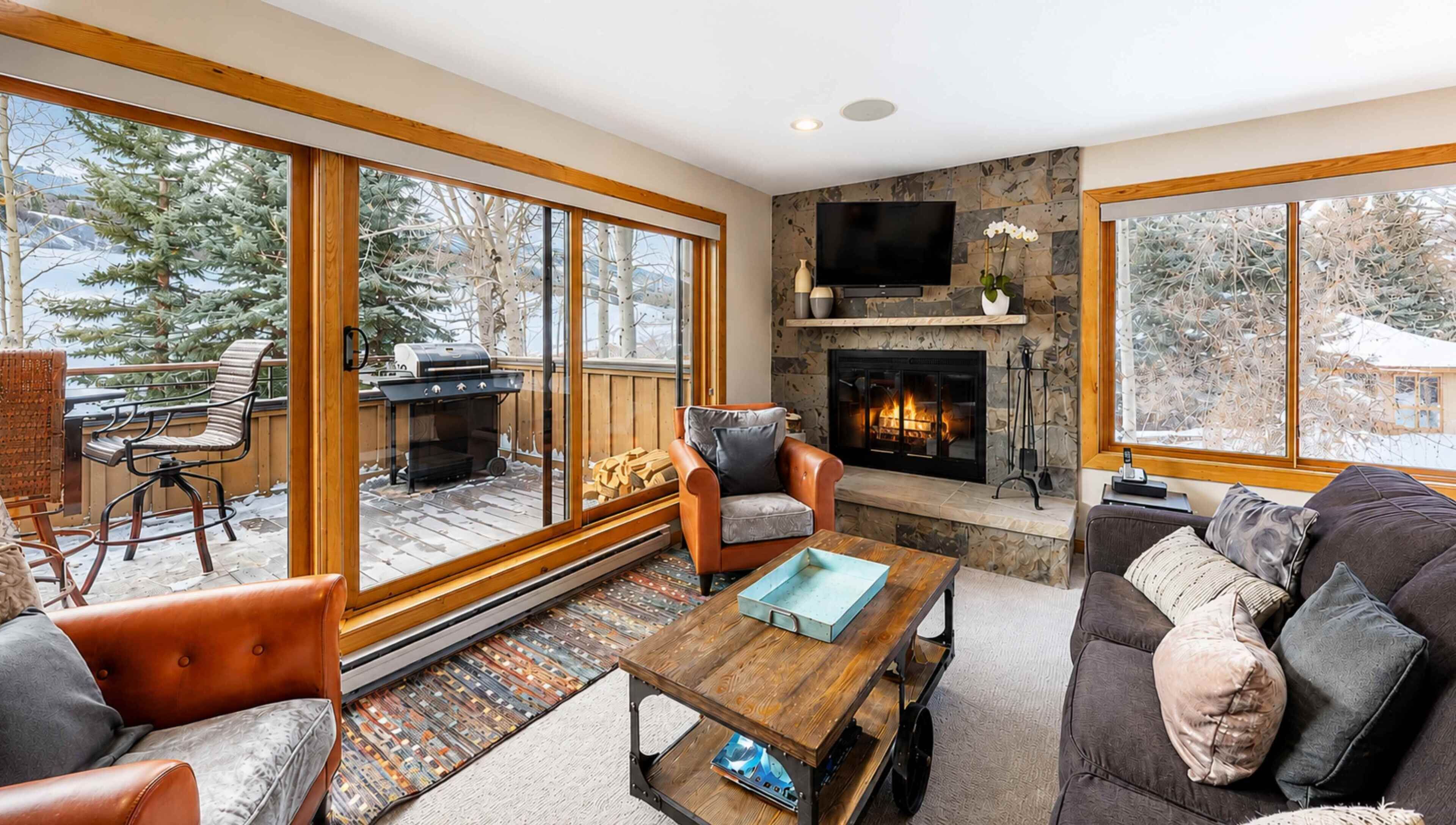 A cozy living room with a fireplace, large windows, and a view of the outdoors.