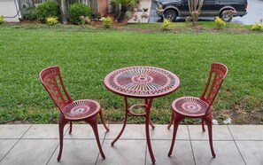 A patio with a round metal table and two chairs, surrounded by a well-maintained lawn and a wooden fence.