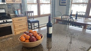 Una cocina con encimera de granito, un bol de madera con fruta y una botella de vino.