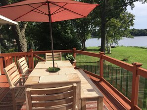 Eine Holzdiele mit Tisch, Stühlen und einem Sonnenschirm, mit Blick auf einen See.