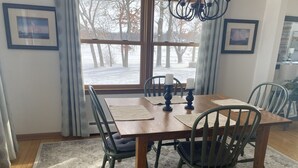 Un comedor con una mesa de madera, cuatro sillas y vistas a un paisaje nevado a través de grandes ventanales.