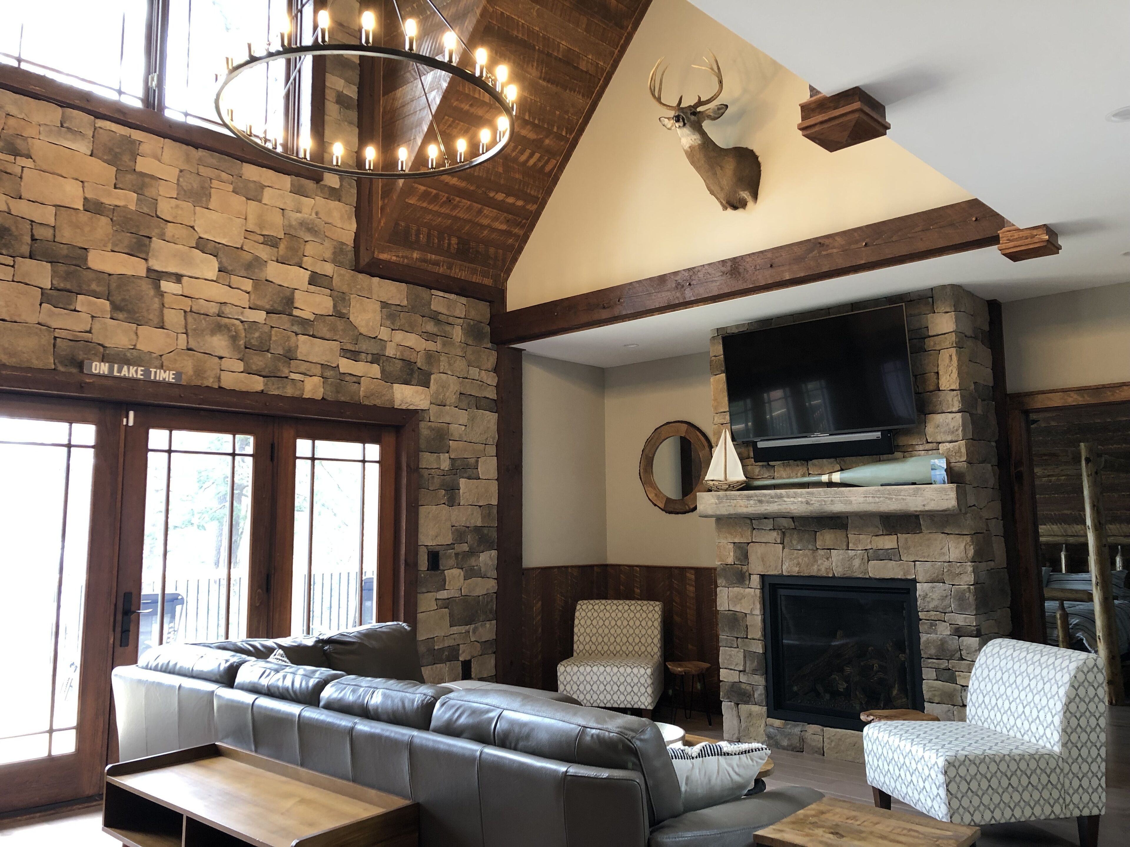 A cozy living room with a stone wall, a fireplace, a mounted deer head, and a leather sofa.