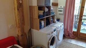 Un espace buanderie comprenant un lave-linge, des étagères avec des serviettes pliées et un radiateur.