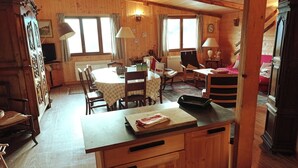 Un intérieur en bois comprenant une table à manger, des chaises, un comptoir de cuisine et un lit recouvert d’une couverture à rayures.