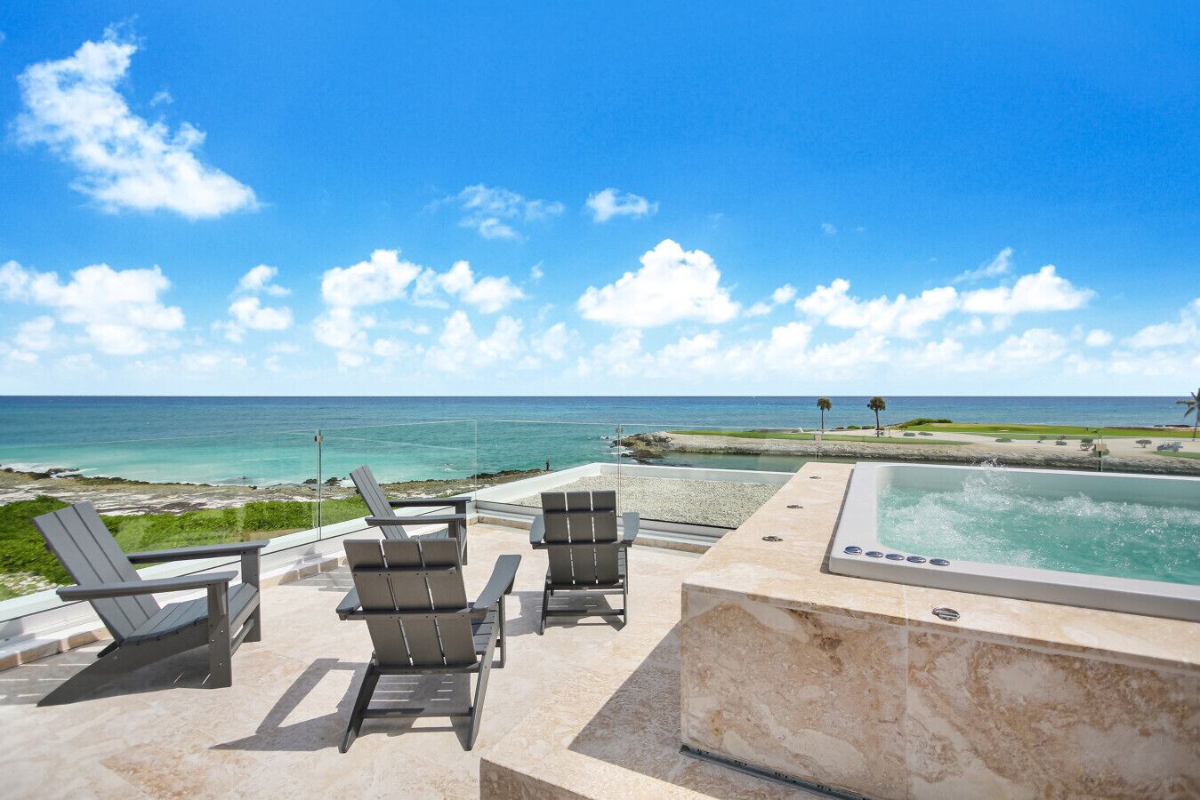 Uma área na beira da piscina com espreguiçadeiras e uma banheira de hidromassagem com vista para o oceano.