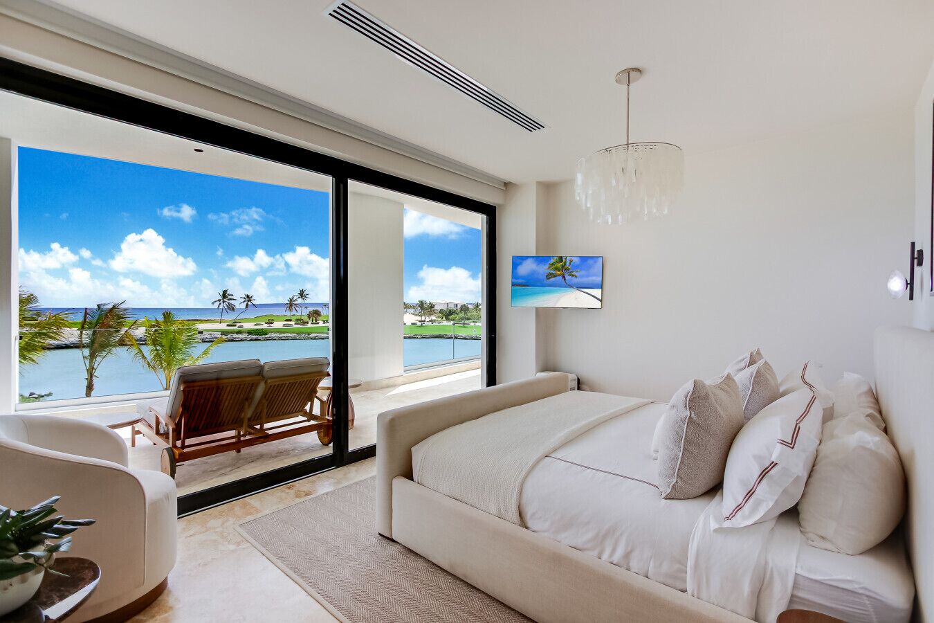 A bedroom with a bed, a TV, and a view of a beach.