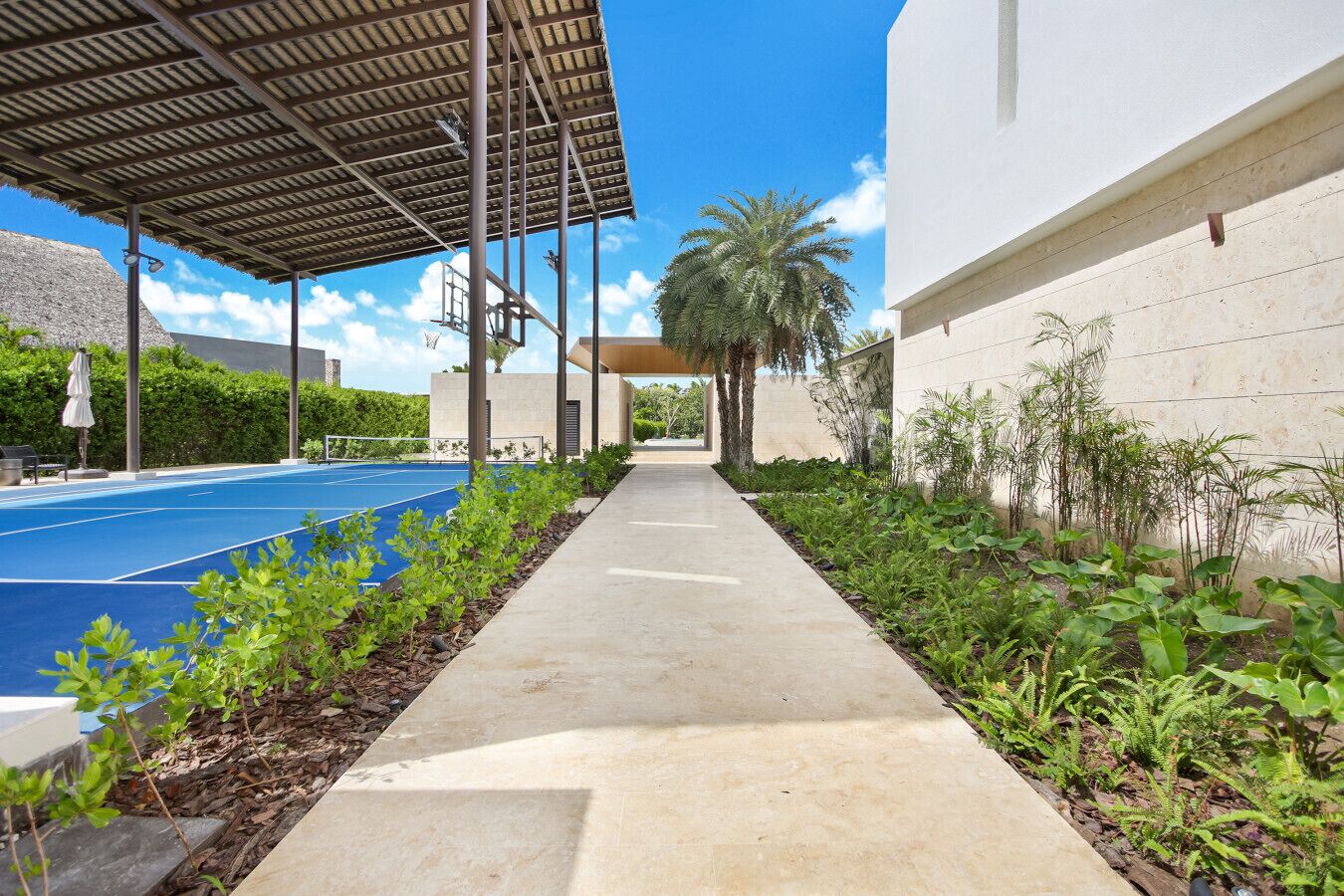 A pathway leading to a pool area with a covered seating area and a building with a white facade.