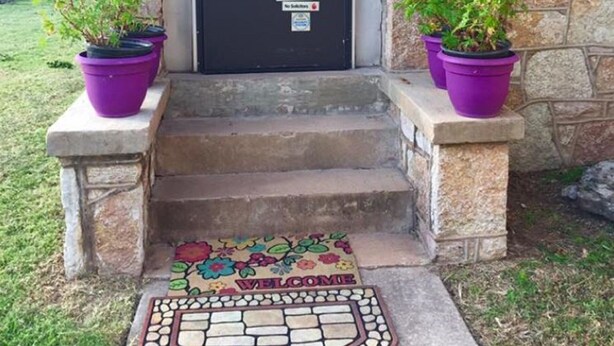A stone building with a black door, two purple potted plants on the steps, and a welcome mat with a floral design. - Hunterston Cottage -Sleeps 6 - Ft. Sill, Wichita Mountains, Casinos (Lawton)