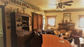 A cozy living room with a fireplace, a bookshelf, and a dining area with a table and chairs. - Hunterston Cottage -Sleeps 6 - Ft. Sill, Wichita Mountains, Casinos (Lawton)