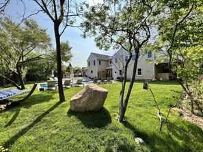 A backyard with a swimming pool, lounge chairs, and a large rock.