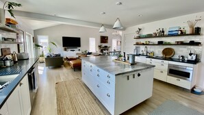 Et moderne køkken med en central ø, hvide skabe og et spiseområde med sofa og sofabord.