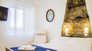 A hotel room with a bed, a chair, a television, and a stone wall with shelves.