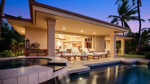 A luxurious outdoor pool area with a waterfall feature, lounge chairs, and a covered patio.