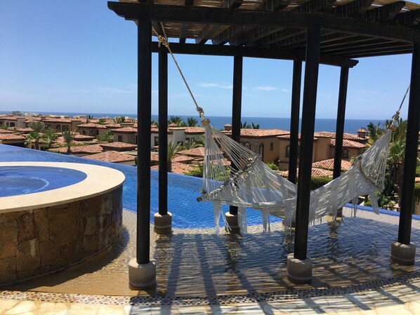 Un espace piscine agrémenté d’un bassin circulaire, de hamacs et offrant une vue sur une ville côtière.