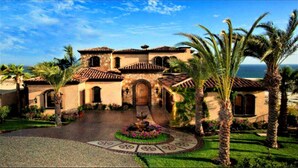 Una villa de estilo mediterráneo con un patio central, palmeras y vistas al océano.