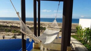 Una hamaca colgada entre vigas de madera, con vista a una playa y un cielo despejado.