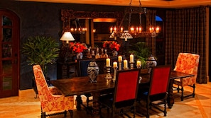 Un coin repas avec une table en bois, des chaises à l’assise rembourrée de couleur rouge et un lustre orné de nombreuses bougies.