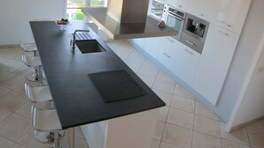 Una cocina moderna con una isla central, armarios blancos y electrodomésticos de acero inoxidable.