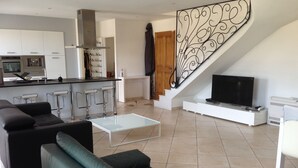 Una sala de estar moderna con un sofá, una mesa de centro, un televisor y una zona de cocina con estufa y taburetes de bar.