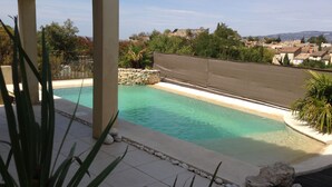 Una piscina con borde de piedra, rodeada por una pérgola y plantas.