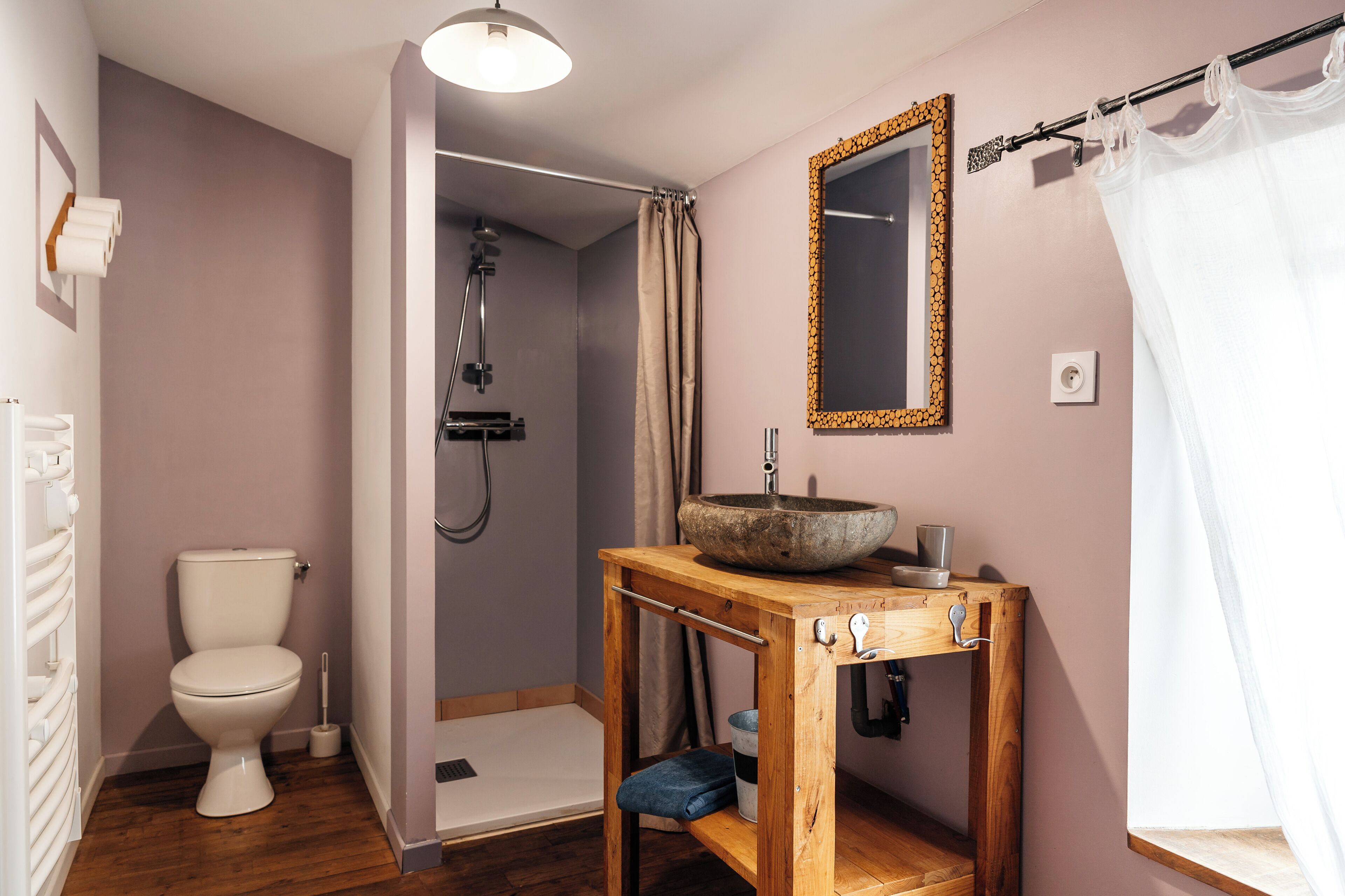 Une salle de bain comprenant des toilettes, un meuble-lavabo en bois avec un évier, une douche et un miroir avec un cadre décoratif.